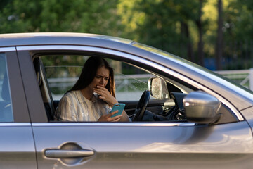 Girl cry reading message in mobile phone. Frustrated upset young woman in tears sit at driver seat in car with smartphone in hand. Female get bad news, breaking up with boyfriend in text sms messenger