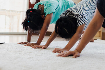 Asian young mother and her daughters doing stretching fitness exercise yoga together at home. Parent and children work out to be strong and maintain physical health and wellbeing in daily routine.