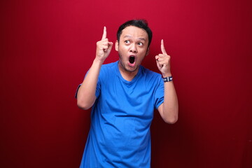 Shock Young asian man is surprised and shouting wow with pointing above with his hand isolated on red background.