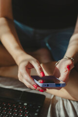 Woman texting using mobile phone, hands with red nail polish manicure in frame. Online shopping.