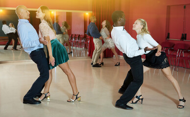 Fototapeta premium Smiling adult pairs dancing tango movements in modern dance studio