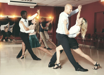 Adult dancing couples enjoying latin dances in modern studio..