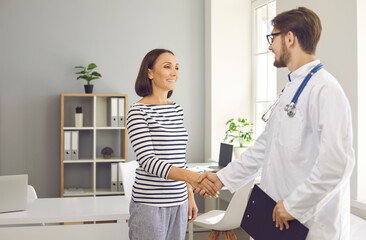 Fototapeta premium Happy smiling patient shaking hands with medical professional in modern clinic or hospital. Friendly physician welcoming mature woman in his office. Healthcare, health checkup, visit to doctor concept