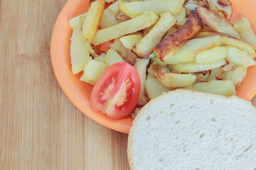 fried potatoes in a plate with a tomato and a piece of bread on a wooden board