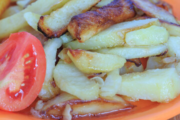 fried potatoes with tomato in a plate on a wooden board macro