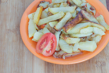 fried potatoes with tomato in a plate on a wooden board top view
