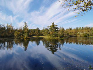 The surface of a forest lake, in which trees with yellow leaves and the sky with beautiful clouds are reflected.