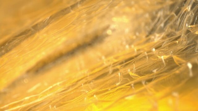RACK FOCUSING from outer edge of bubble wrap bag, macro view of several air pockets. DEFOCUSED as it shifts to the end of the bag and then back again. The bag lit yellow and gold lighting