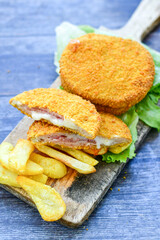 
 Crispy  deep fried home made     chicken Cordon bleu with cheese   and ham  and french fries on wooden rustic background.  
