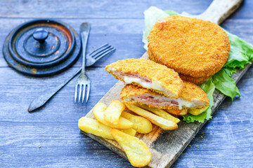 
 Crispy  deep fried home made     chicken Cordon bleu with cheese   and ham  and french fries on wooden rustic background.  