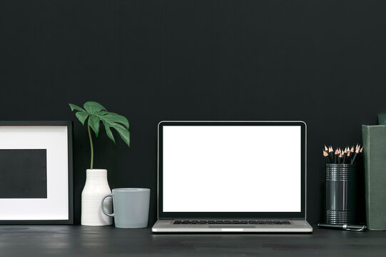 Creative workspace with blank screen laptop computer and stationary in dark tone color style.