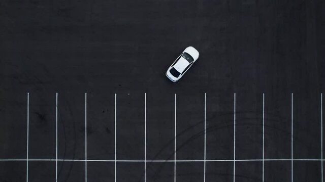 Aerial view of a white car pulling out of a parking space. Empty parking lot. Smooth white markings in the parking lot