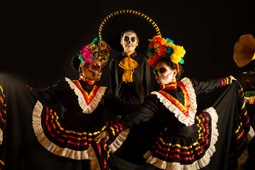 people dressed in Mexican folkloric black and very colorful costumes, with ornaments referring to the Day of the Dead, skull make-up
