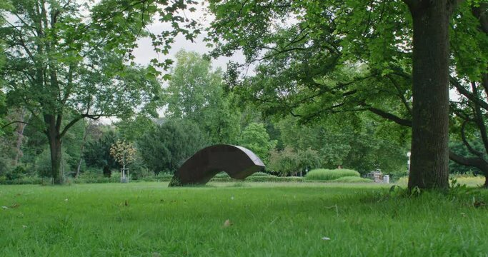 Wide shot of an art installation in the great park of Ulm. Camera tracks forward. Low angle shot with deep depth of field.