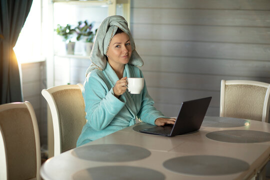 woman after shower, in the morning, with a cup of coffee working with a laptop