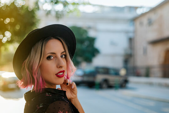 Portrait of young blonde with black hat and pink highlights.