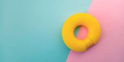 Yellow pop tube. Anti stress sensory plastic toy on blue and pink background. Fidget corrugated poptube. Top view, flat lay, copy space.