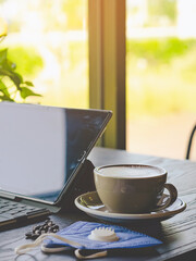 Hot Cappuccino coffee with protective face mask for people work from home by using laptop and stress relief with hot coffee on a table. Concepts of Covid-19 (Coronavirus). Selective focus on coffee.