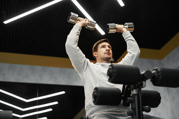 Determined handsome young male working out in gym with dumbbells