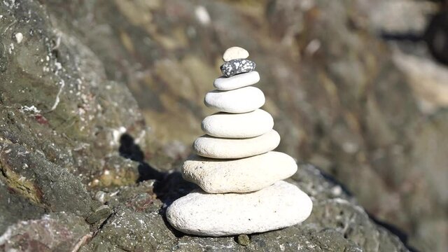 Man bilds stones pyramid on the seashore on a sunny day on the blue sea background. Happy holidays. Pebble beach, calm sea, travel destination. Concept of happy vacation on the sea, meditation, spa