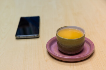 porcelain red tea cup in in plate on on the table with Backlight in afternoon. blurred black mobile phone in background