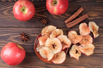 Top view of apple chips and cinnamon and red apples on a wooden table.