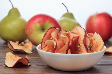 Close-up view of apple chips in the plate and red apples on a wooden table.