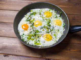 Fried eggs in a frying pan on a plank background. Delicious breakfast. View from above