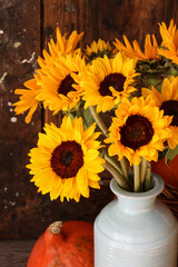 Bouquet of sunflowers in a ceramic vase and orange pumpkins around it.