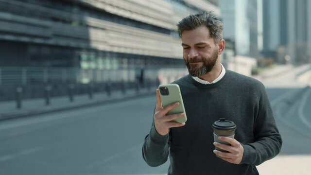 Smiling businessman walking with coffee and mobile in hands