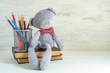 Back to school concept with plush bear, colorful pencils, book stack on white wooden background...