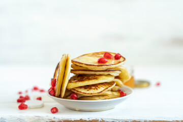Miniature pancakes with fresh honey and pomegranate seeds over white wooden background with copy space.
