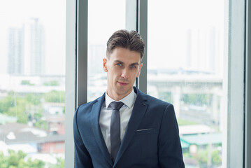 Portrait of smart confident business man standing in front of window with city metropolis background