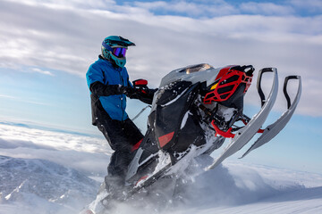 a snowmobiler rides and jumps in the snowy mountains. prof pilot of a mountain snowmobile in bright gear without brands for travel advertising - obrazy, fototapety, plakaty