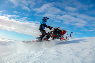 Fotobehang a snowmobiler rides and jumps in the snowy mountains. prof pilot of a mountain snowmobile in bright gear without brands for travel advertising © Wlad Go