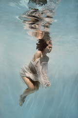 A girl in a blue dress swims underwater on a light background as if in weightlessness