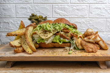Sandwich with fried fish and potato chips over wooden tray.