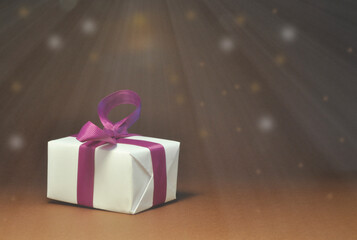 Paquet cadeau blanc, ruban violet. Arrière-plan brun foncé, étoilé.