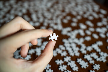 Left hand holding a piece of white jigsaw puzzle