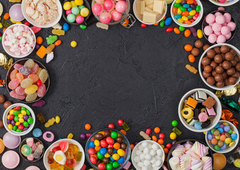 Pink lollipop candies in jar with various milk chocolate and jelly gums candies on black background with liquorice allsorts and strawberry bonbons and large variety of sweets and candies.
