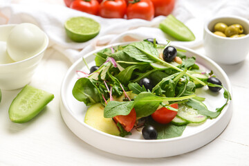 Plate with fresh salad with olives on light wooden background