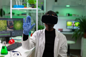 African american biologist woman wearing virtual reality headset working at microbiology experiment...