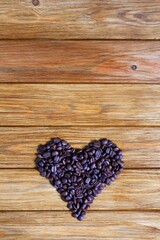 Heap of roasted coffee beans in the shape of a heart on a wooden background