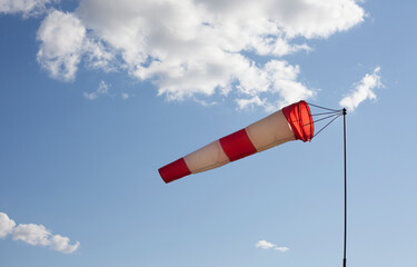 White and red wind flag (windsock) with blue sky background. Air sleeve on a sunny day indicating...