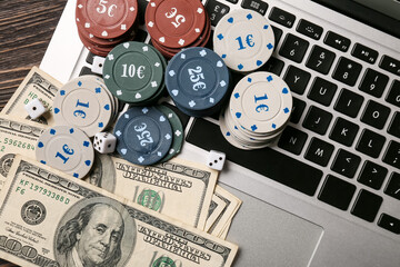 Dices, poker chips, dollar banknotes and laptop on table, closeup