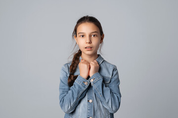 preteen girl looking at camera with nervous and scared facial expression, isolated on grey background, wearing in denim jacket