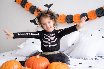 funny caucasian kid girl in witch costume having fun in decorated for halloween bedroom