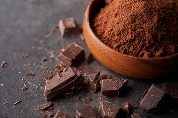 Cocoa powder in bowl and pieces of dark chocolate on a dark grey counter