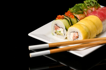 Plate with tasty sushi rolls and chopsticks on dark background, closeup