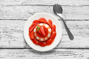 Delicious panna cotta with strawberry and mint in plate on light wooden background